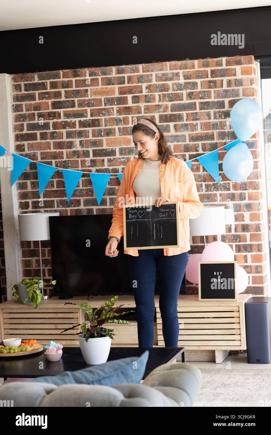 Femme tenant un tableau à la fête de révélation de genre, souriant et célébrant à l'intérieur Banque D'Images