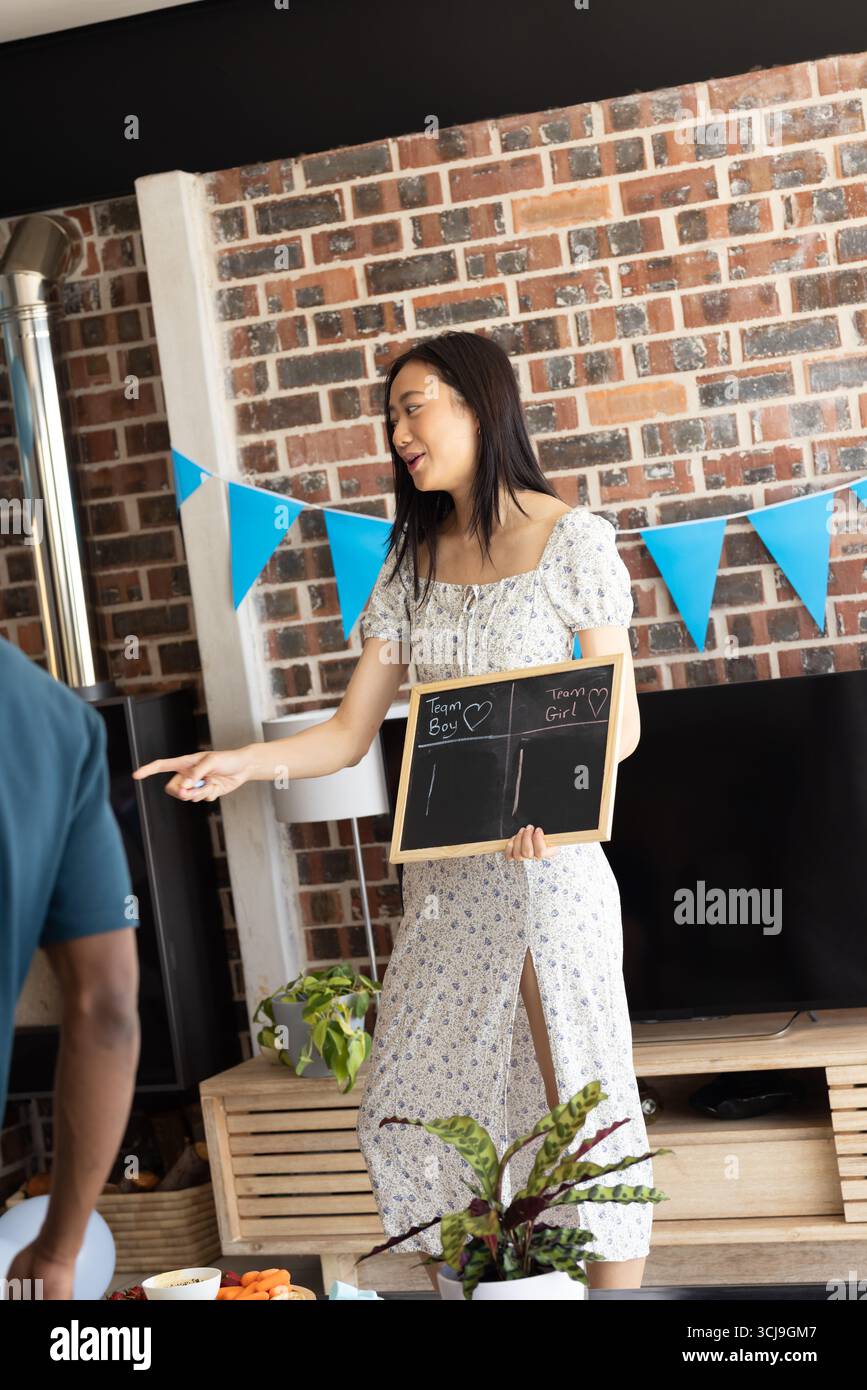 Femme tenant un tableau à la fête de révélation de sexe, souriant et pointant avec excitation Banque D'Images
