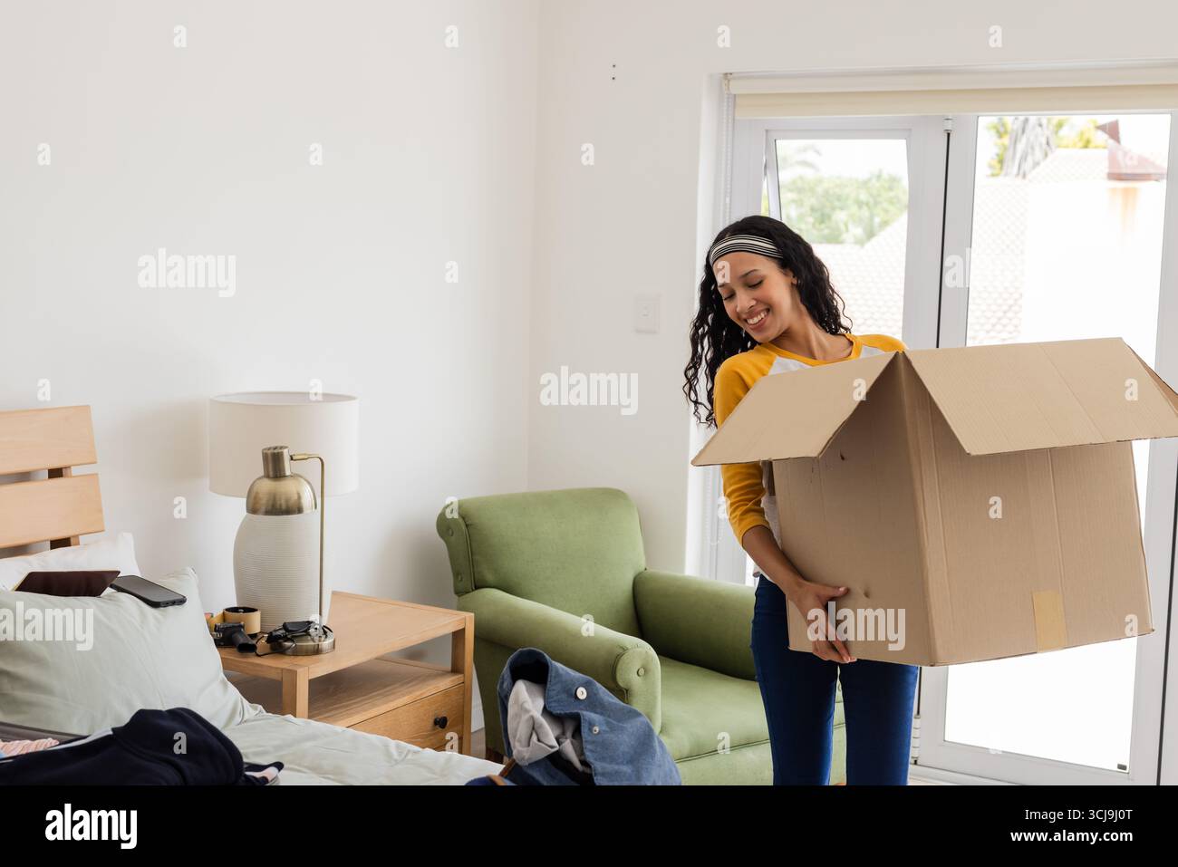 Déballage de la boîte en carton dans la chambre, femme afro-américaine organisant les affaires, souriant Banque D'Images