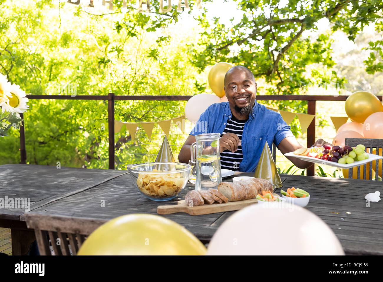 Homme afro-américain adulte assis à la table de patio avec des ballons de chips de pichet d'eau citron Banque D'Images