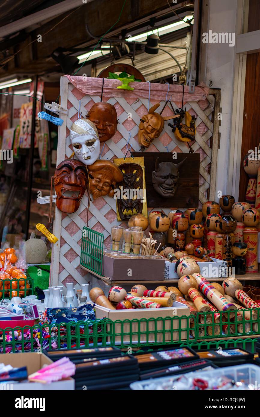 Vitrine de masques japonais traditionnels et de poupées kokeshi en bois sur un stand de marché de rue. Artisanat artisanal coloré et souvenirs culturels en vente. Banque D'Images
