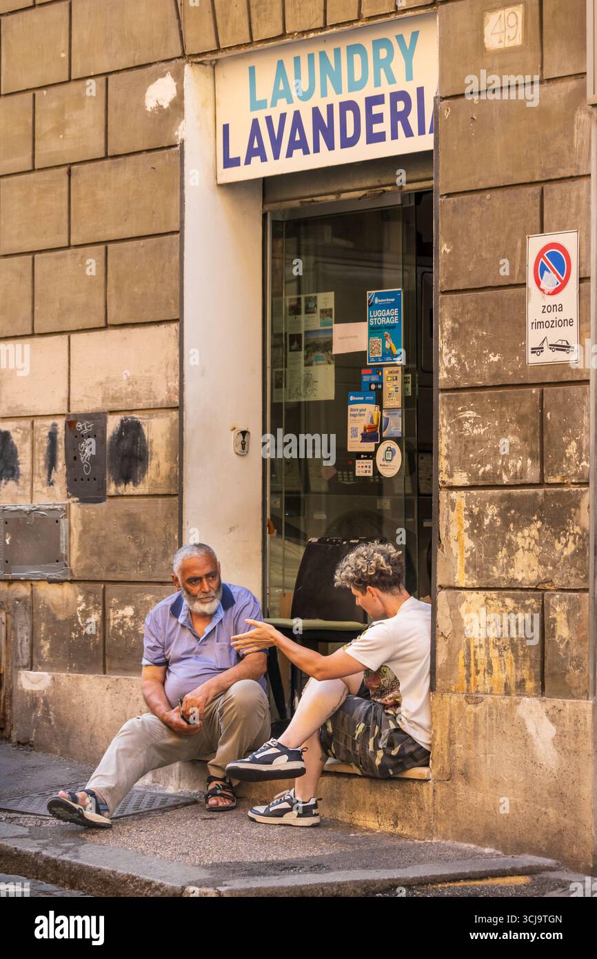Deux amis parlant devant un magasin de nettoyage à sec Rome, Italie 07-14-2025 Banque D'Images