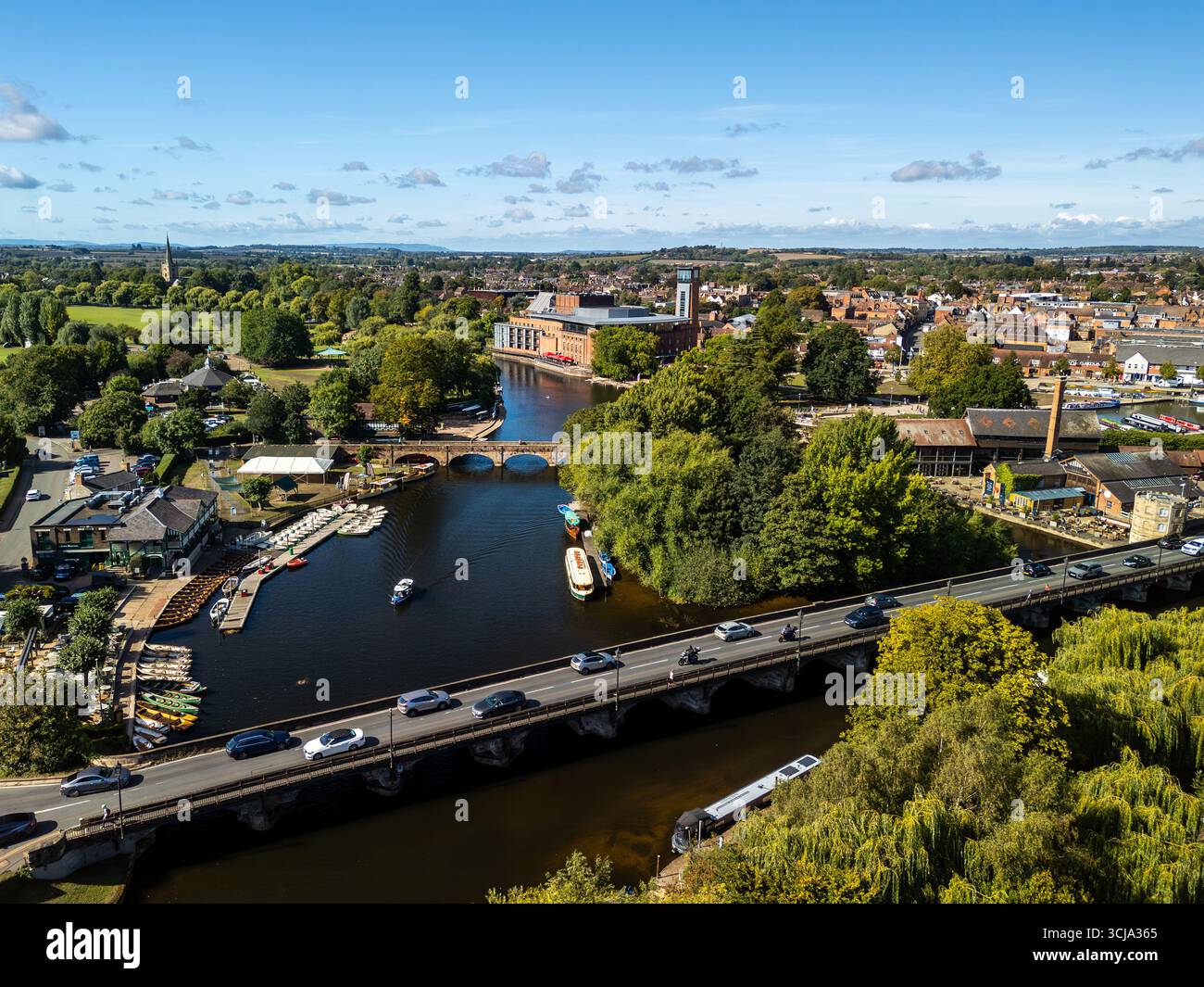 Voitures traversant le pont sur la rivière Avon à Stratford-upon-Avon, Warwickshire, Angleterre, avec des bateaux amarrés le long de la rivière et des bâtiments Banque D'Images