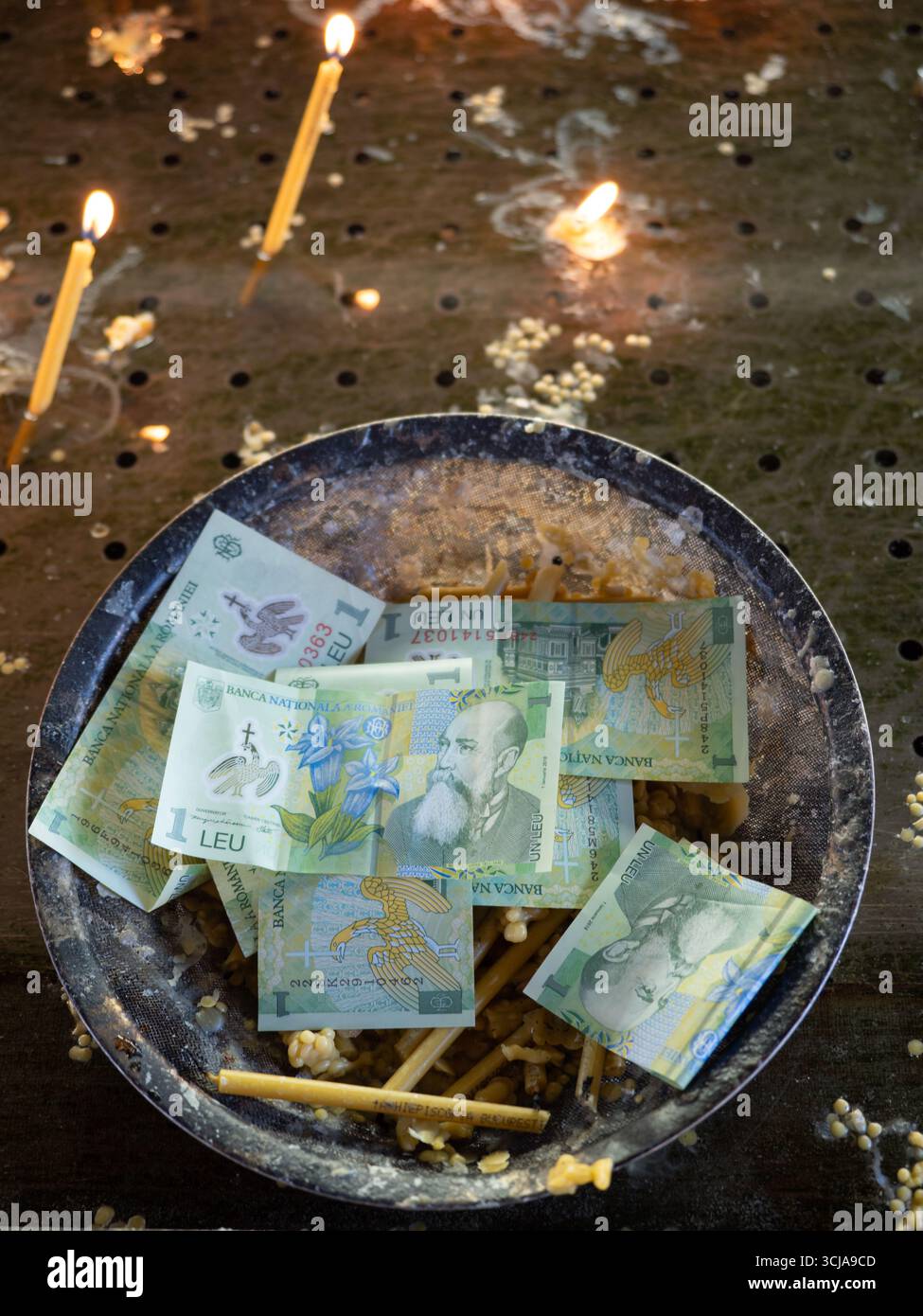 2025-08-24 Sinaia, Roumanie : éditorial seulement. Billets de banque roumains de 1 Leu placés dans un bol de don avec des bougies allumées en arrière-plan. Banque D'Images