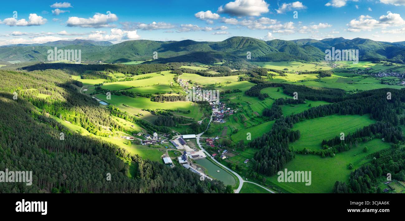 Paysage serein avec le village rural. des prairies verdoyantes hurlantes, des maisons traditionnelles et des montagnes alpines pittoresques sous un sk bleu clair Banque D'Images