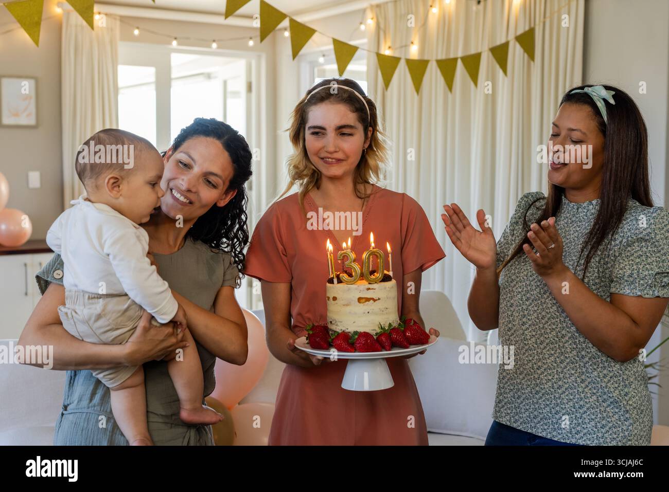 Célébrant l'anniversaire, femme tenant le gâteau avec des bougies tandis que les amis applaudissent et sourient Banque D'Images