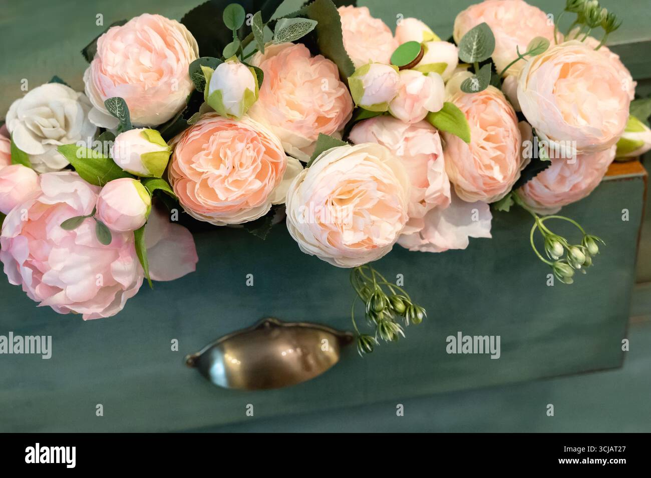 Un magnifique arrangement floral avec des roses roses roses douces et une verdure délicate placés élégamment sur un fond sarcelle, parfait pour la décoration d'intérieur ou l'événement s. Banque D'Images
