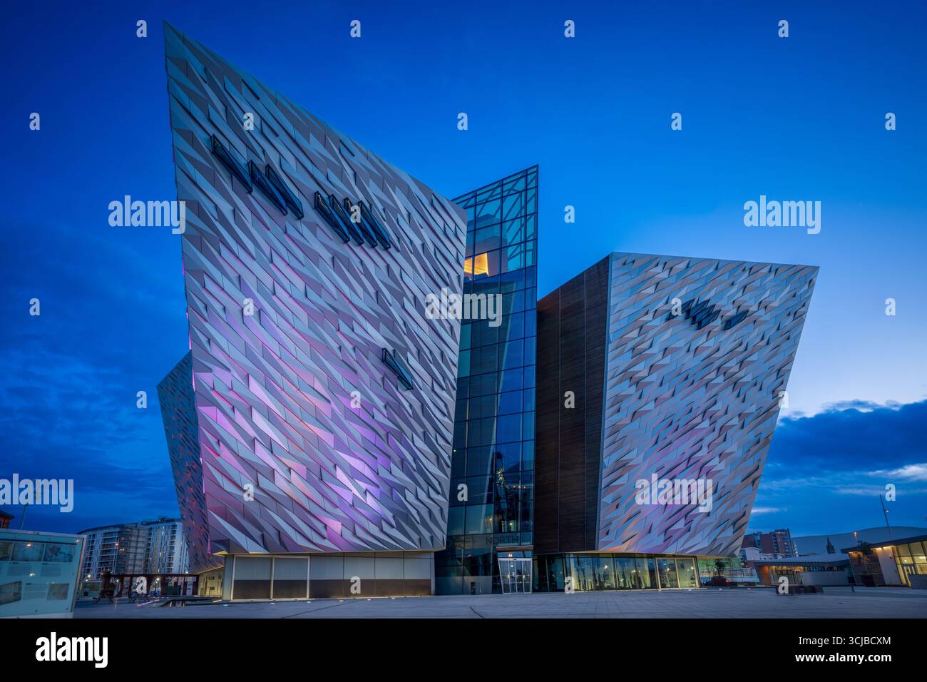 Vue en soirée du Titanic Belfast Museum illuminé pendant l’heure bleue, avec une architecture moderne reflétant le patrimoine maritime de la ville. Banque D'Images
