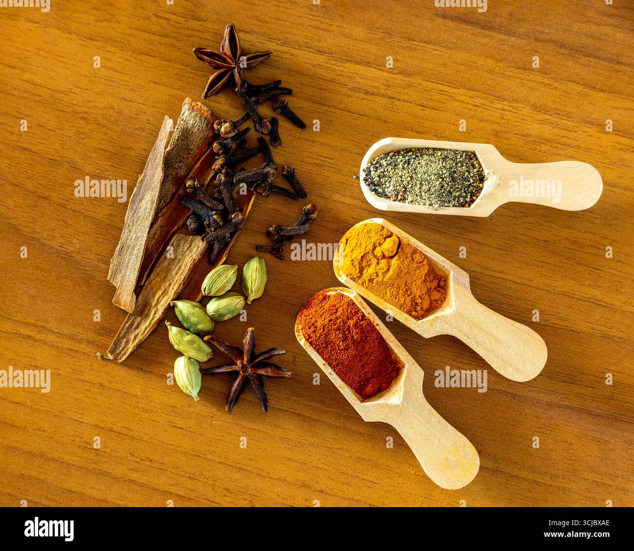 Épices entières les bols contiennent des clous de girofle, des gousses vertes de cardamome et des graines de fenugrec. Dispersés sur la surface sont des grains de poivre noir, de l'anis étoilé et du cinn Banque D'Images