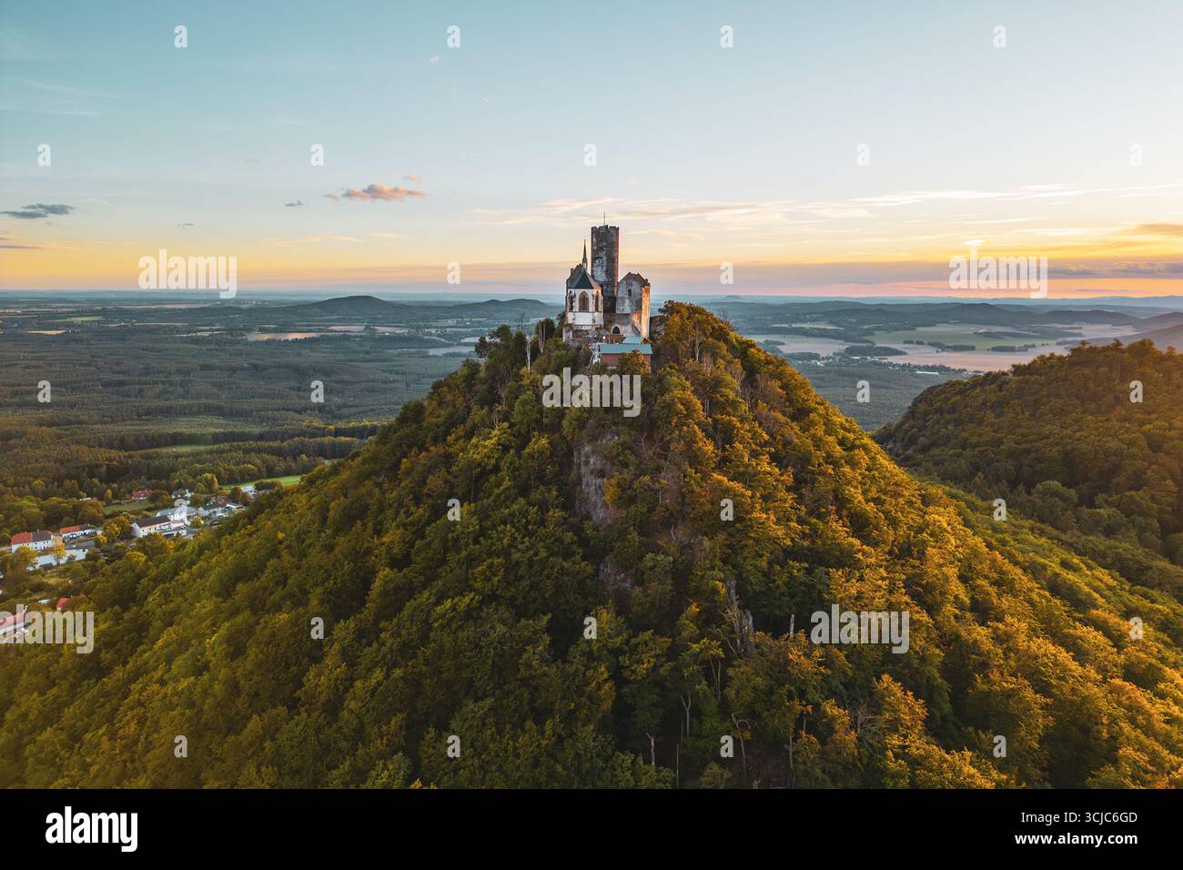 Le château de Bezdez se dresse majestueusement sur un pic rocheux entouré d'une végétation luxuriante pendant l'heure dorée de l'été. Le soleil se couche derrière la structure médiévale, renforçant son charme historique et sa beauté. Banque D'Images