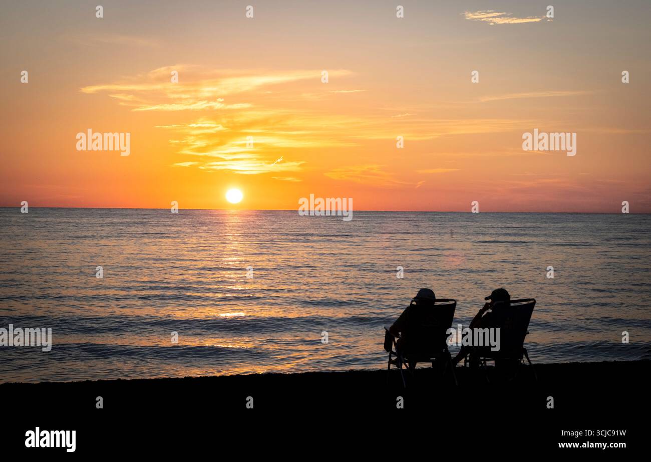 Couple assis sur la plage regardant le coucher du soleil sur le golfe d'Amérique, anciennement le golfe du Mexique, de Vencie Beach à Vencie Florida USA Banque D'Images