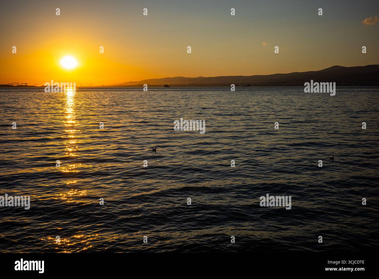 Le soleil se couche sur le golfe d'Izmit, projetant des reflets dorés sur l'eau avec des montagnes lointaines et des bateaux visibles à l'horizon à Kocaeli, Turki Banque D'Images