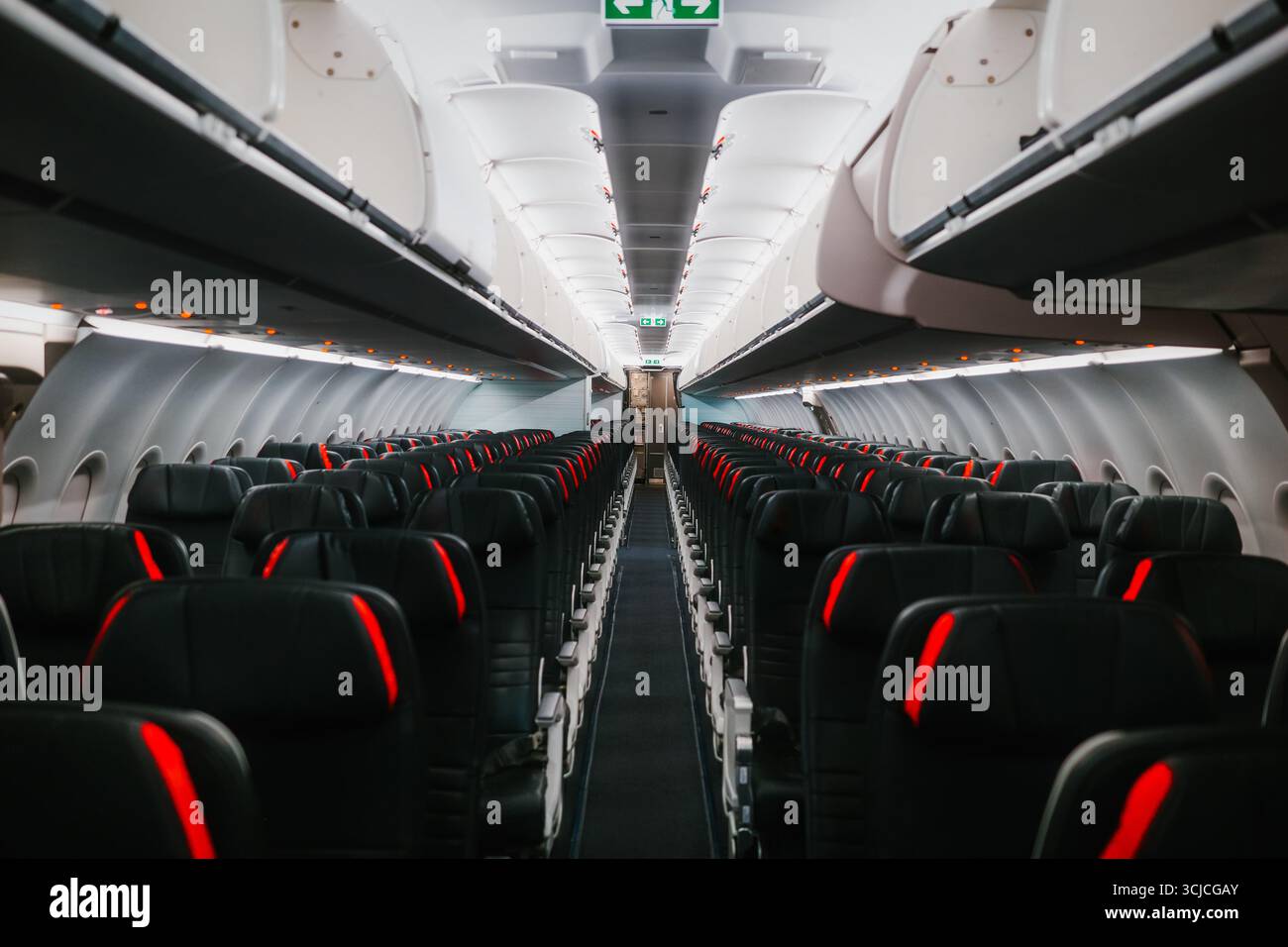 Vue d'une cabine d'avion commercial vide montrant des rangées de sièges noirs avec des accents rouges. Les compartiments supérieurs sont fermés et aucun passager n'est présent Banque D'Images