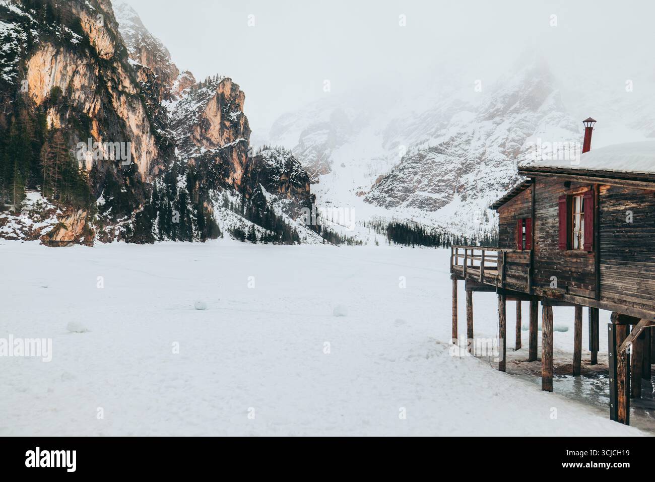 Une superbe scène hivernale dans les Dolomites, en Italie, mettant en vedette une cabane rustique à côté d'un lac gelé, entourée de montagnes enneigées et de pins U. Banque D'Images