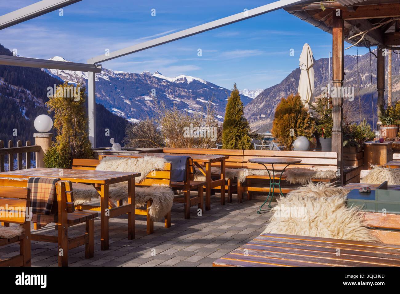 Un restaurant autrichien accueillant en terrasse situé dans les Alpes enneigées en hiver. Des bancs en bois confortables avec des jetés de fourrure offrent chaleur et charme contre une race Banque D'Images