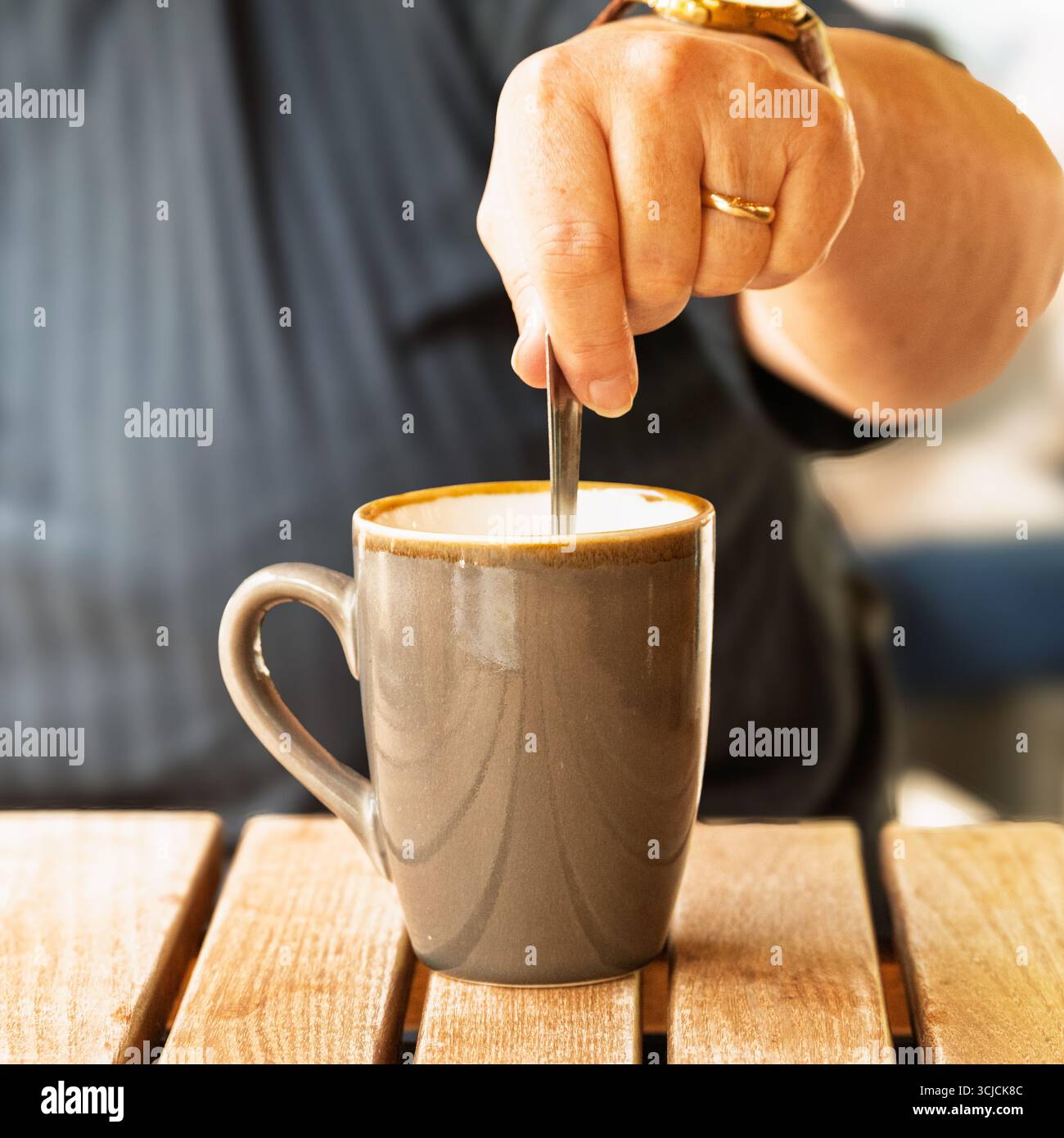 Remuer une boisson chaude. Une personne remue une boisson, probablement du café ou du thé, pour la mélanger au sucre ou à la crème. Banque D'Images