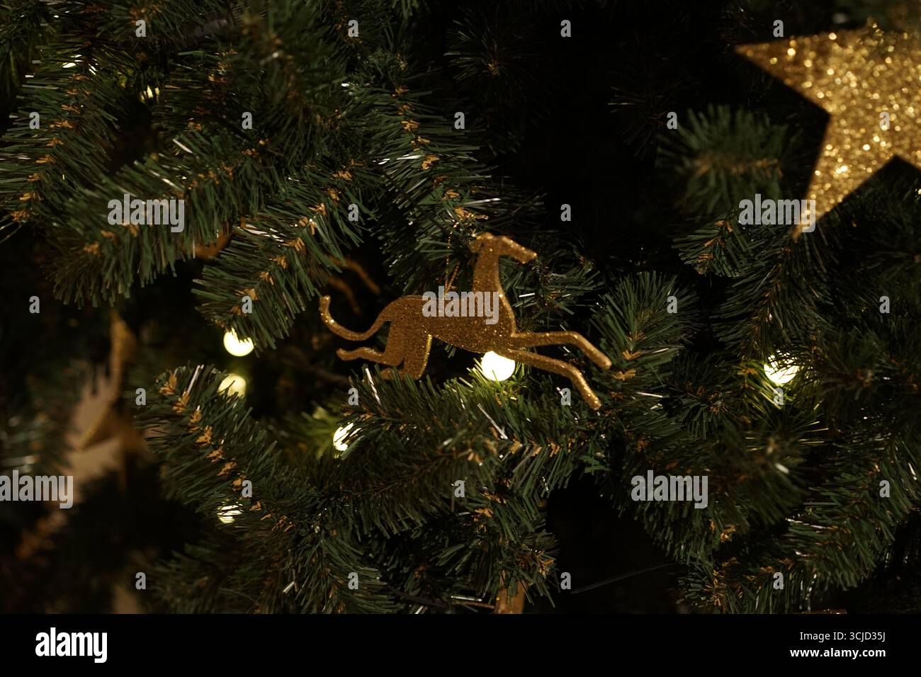 Un ornement de cheval en or orne un sapin de Noël, entouré d'accents rouge foncé et noir, évoquant le luxe et l'atmosphère festive Banque D'Images