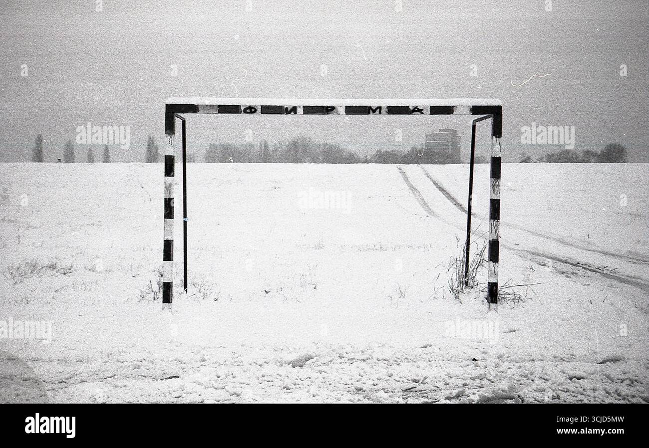 Photographie noir et blanc à contraste élevé de terrains de handball et de football recouverts de neige, avec un seul poteau de but visible dans le cadre. Banque D'Images