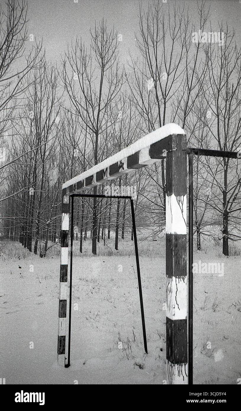 Photographie noir et blanc à contraste élevé de terrains de handball et de football recouverts de neige, avec un seul poteau de but visible dans le cadre. Banque D'Images