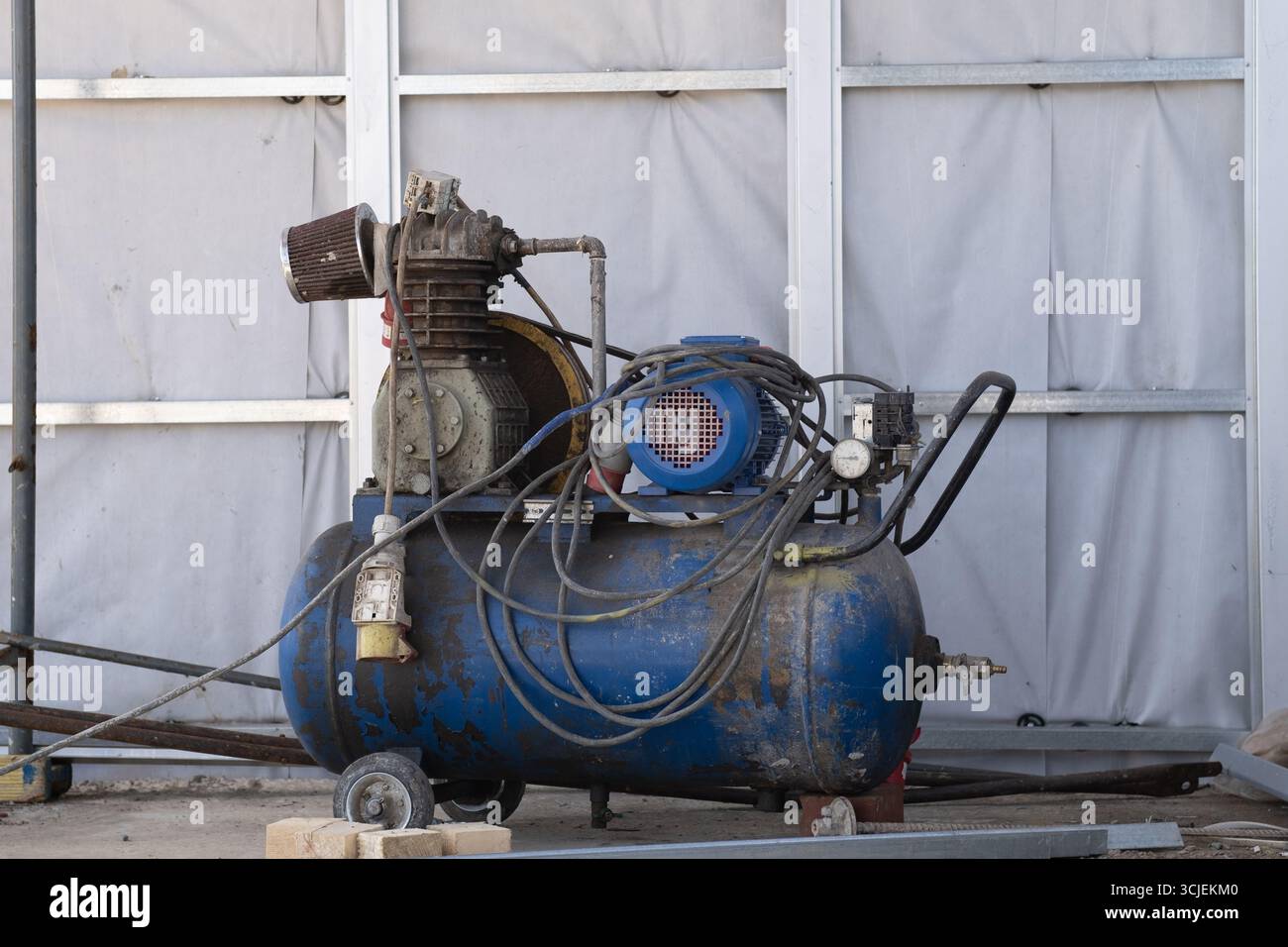 Un vieux compresseur d'air mobile de travail bleu pour peindre les murs sur un chantier de construction. Matériel d'ingénierie. Banque D'Images