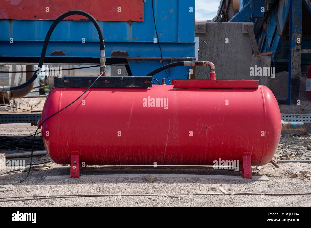 Grand réservoir rouge de compresseur d'air industriel avec des tuyaux connectés sur le chantier de construction extérieur avec le béton et le fond de machines Banque D'Images