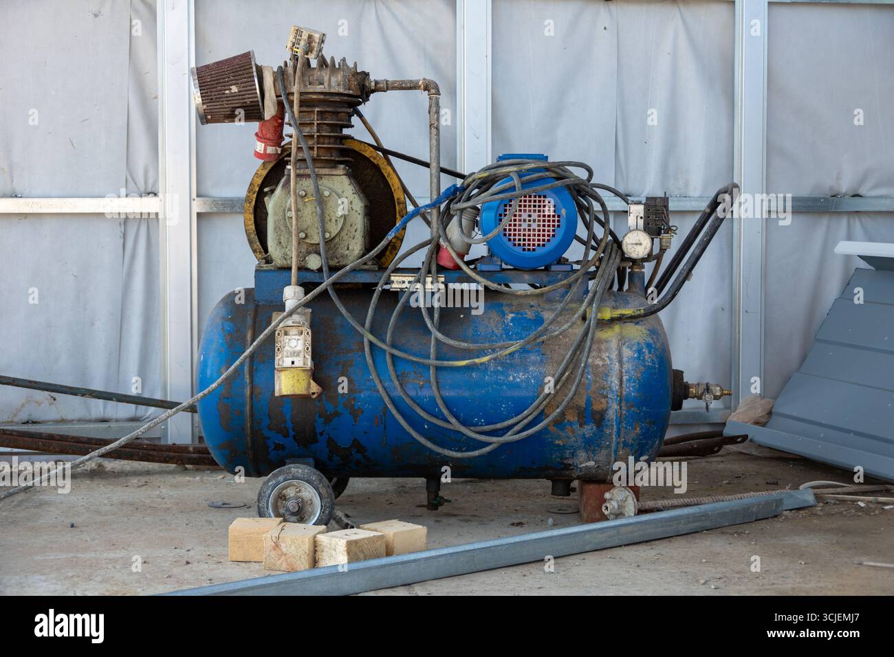 Un vieux compresseur d'air mobile de travail bleu pour peindre les murs sur un chantier de construction. Matériel d'ingénierie. Banque D'Images