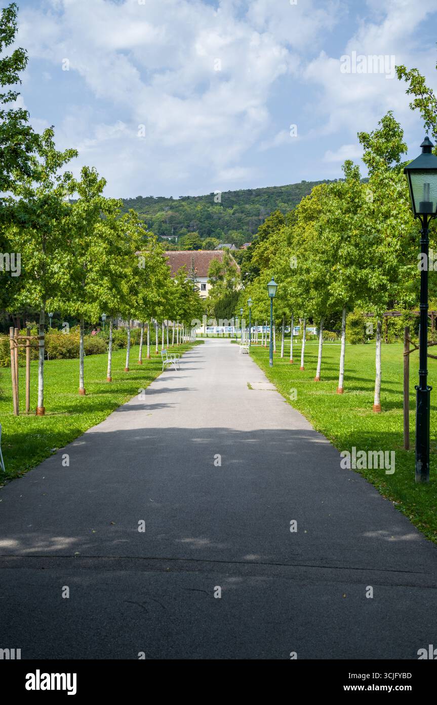 Un sentier paisible bordé d'arbres et de bancs invite les visiteurs à se promener et à se détendre. Le paysage soigné offre une escapade paisible hors de la ville Banque D'Images