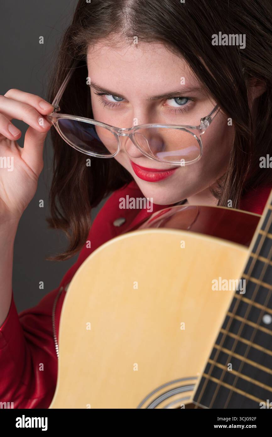 Musicienne avec guitare regarde la caméra tout en abaissant ses lunettes et en les tenant par sa tempe avec une main Banque D'Images
