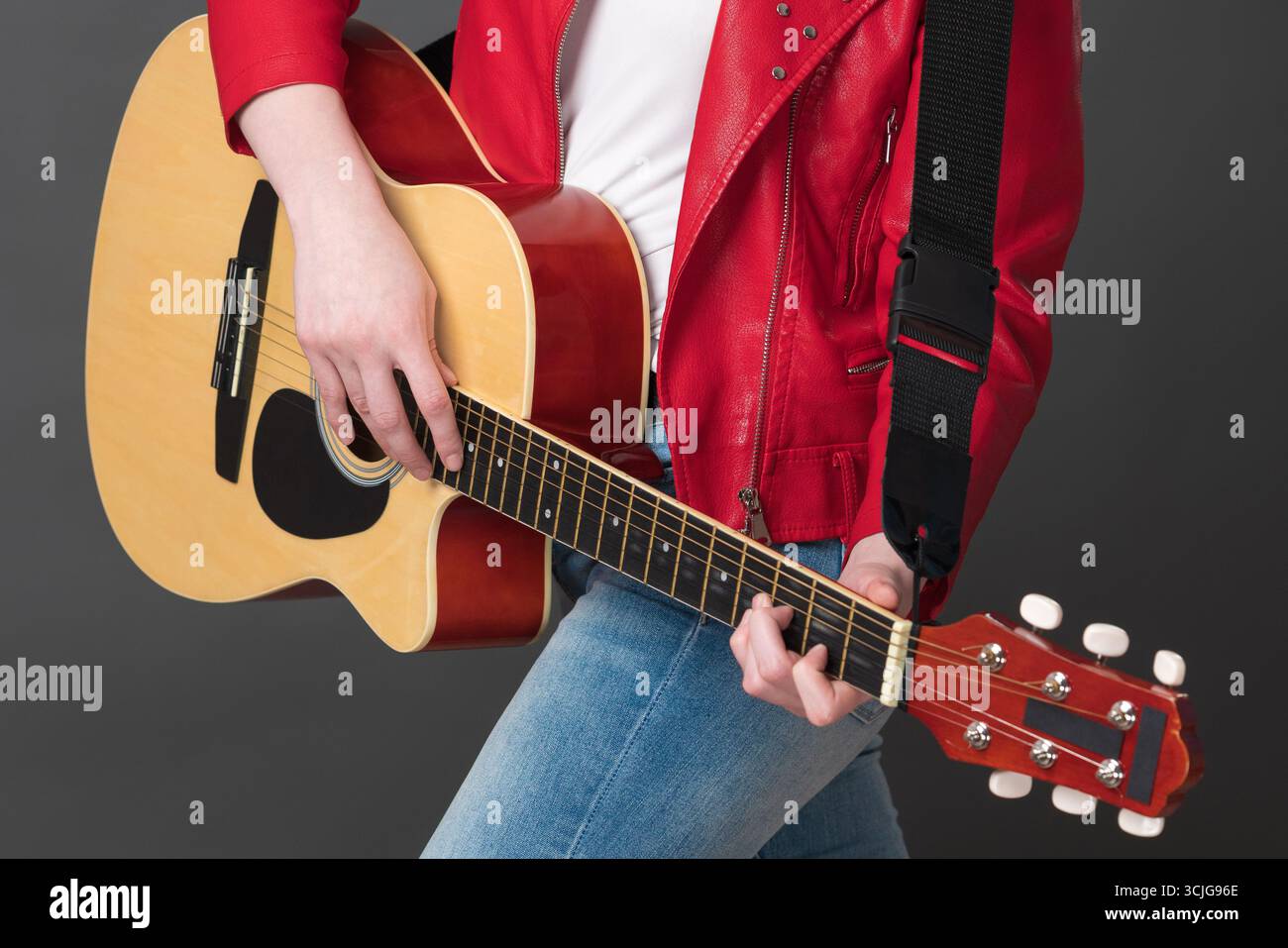 Guitariste femme méconnaissable jouant de la guitare acoustique avec concentration. Vue rognée de la section médiane d'une musicienne rock élégante habillée en l rouge Banque D'Images