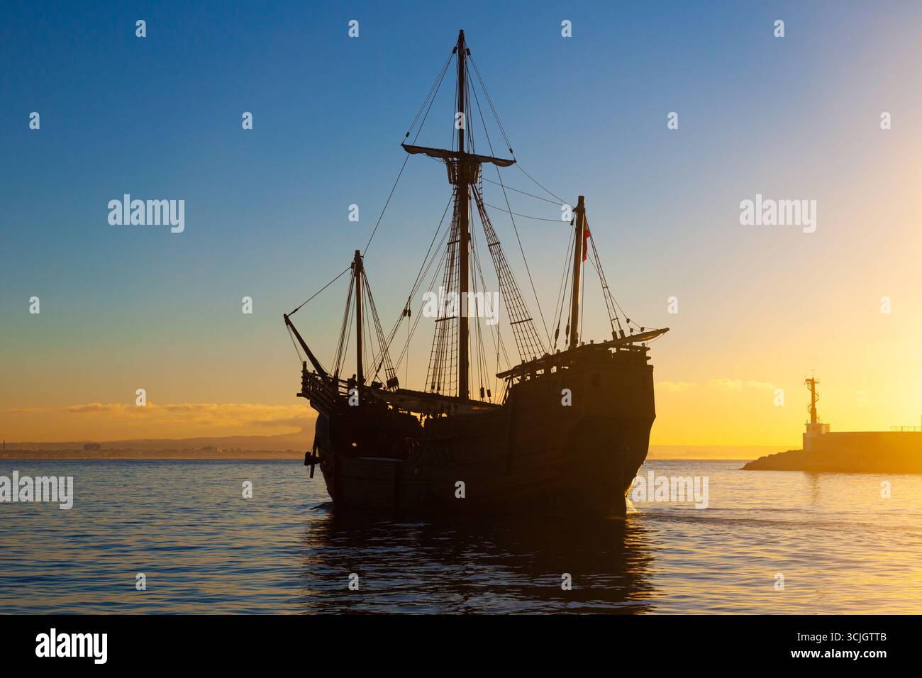 Une vieille caravelle en bois avec des voiles pliées quittant la baie de la mer au coucher du soleil à l'heure bleue. Banque D'Images