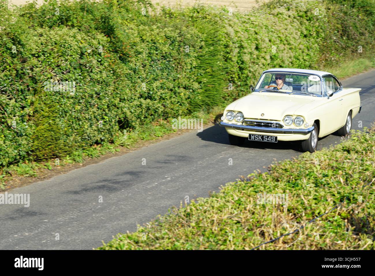 Vintage jaune voiture classique sur une route de campagne entourée de verdure. Shere Hill Climb, East Clandon, Guildford Banque D'Images