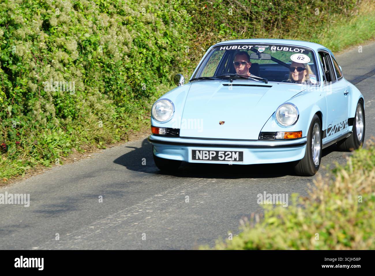 Voiture bleue vintage avec deux passagers conduisant sur une route panoramique. Shere Hill Climb, East Clandon, Guildford Banque D'Images