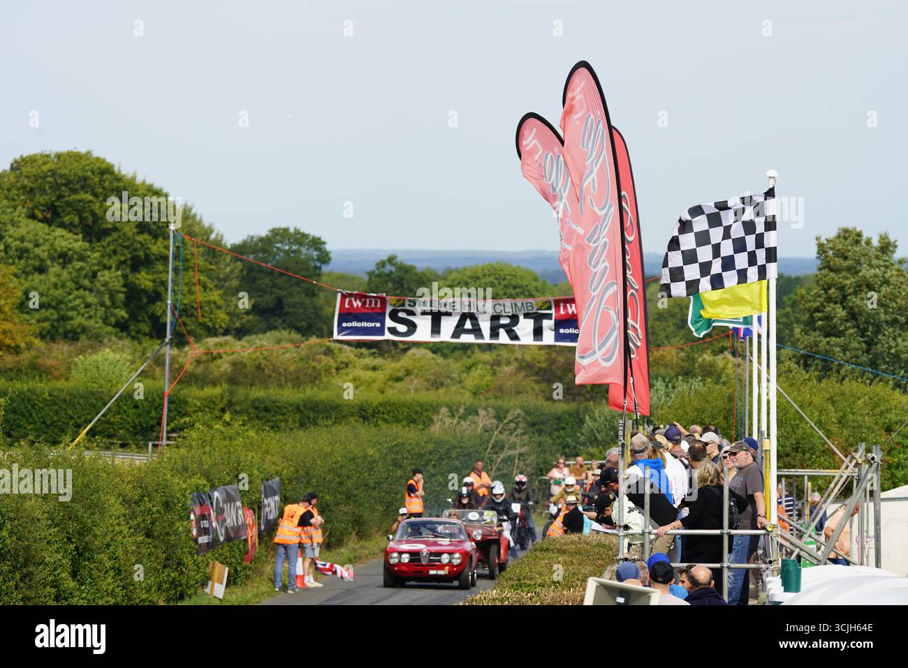 Départ de la course de voitures anciennes avec foule et drapeaux vibrants affichés. Shere Hill Climb, East Clandon, Guildford Banque D'Images