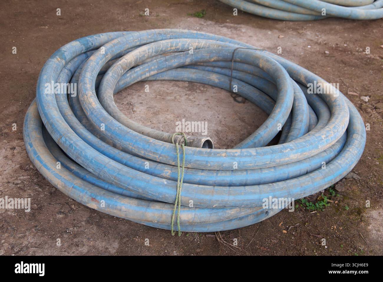 tuyau robuste bleu enroulé couché sur le sol extérieur, se connecte au compresseur et à la perceuse dans l'industrie des puits tubulaires, soft focus dans le flou Banque D'Images