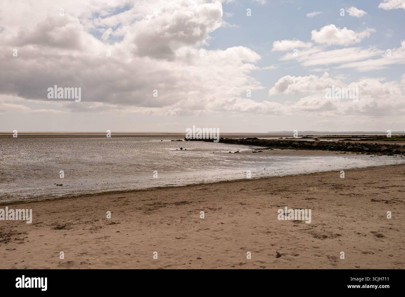 Une plage avec un ciel nuageux en arrière-plan. Le ciel est principalement nuageux avec quelques taches de bleu. La plage est la plupart du temps vide avec seulement quelques personnes vis Banque D'Images