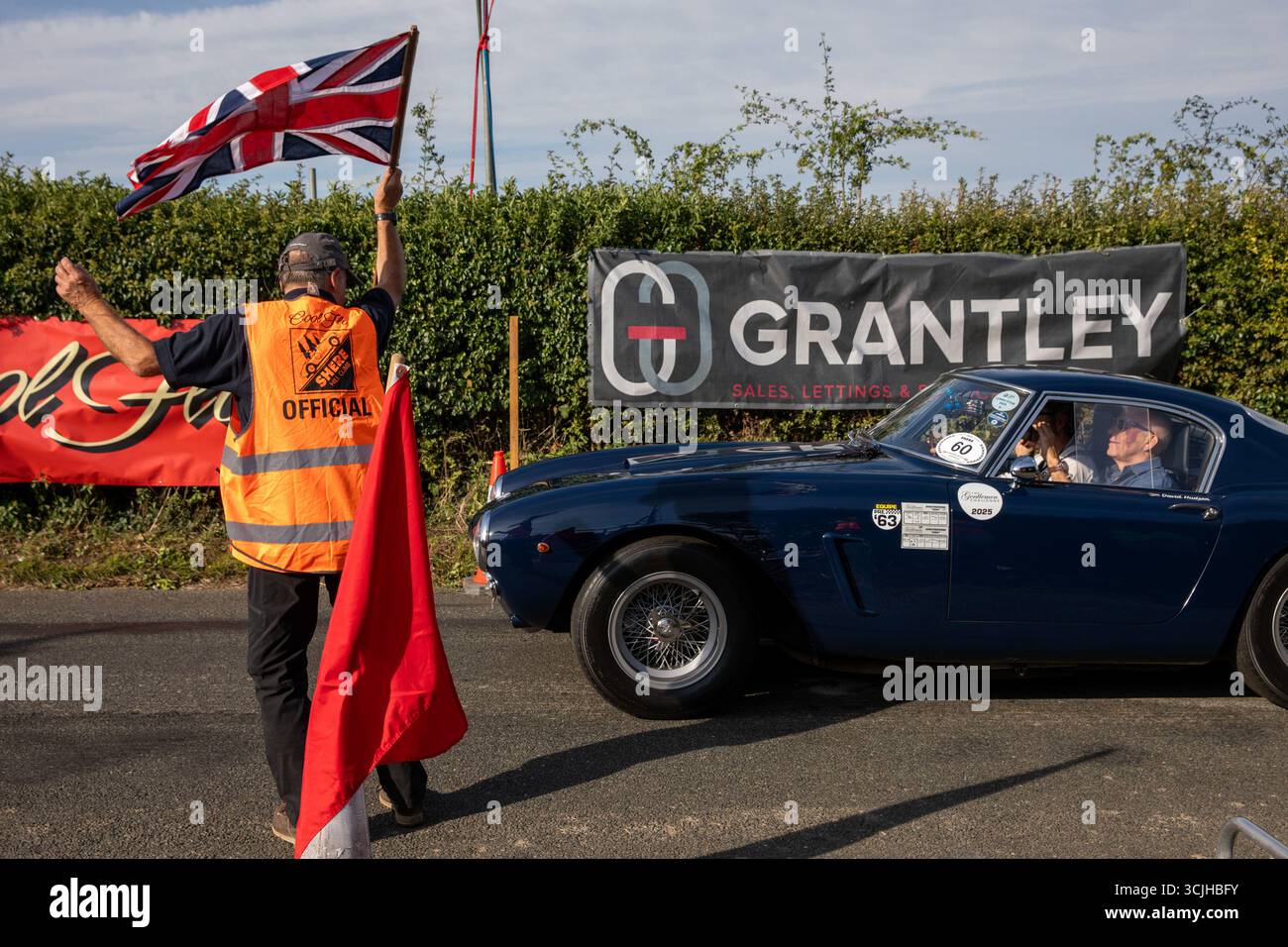 Guilford, Royaume-Uni. 07 septembre 2025. Un démarreur agite un drapeau pour lâcher une Ferrari 250 GT SWB en montée. La 13e ascension de Shere Hill a attiré des centaines de passionnés d'automobile. Cet événement automobile annuel met en vedette des participants du public conduisant des véhicules standard, ainsi que des propriétaires de voitures de course, classiques et supercars, qui concourent sur une voie publique fermée pour obtenir le meilleur temps contre la montre. Outre la montée de la colline, les concurrents et les spectateurs ont eu la chance de voir les voitures concurrentes dans la grande zone de paddock à la ligne de départ du parcours. Crédit : SOPA images Limited/Alamy Live News Banque D'Images