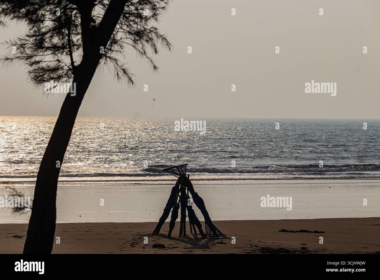 Cadre de filet de pêche altéré jetant une longue ombre sur la plage ensoleillée matin. Banque D'Images