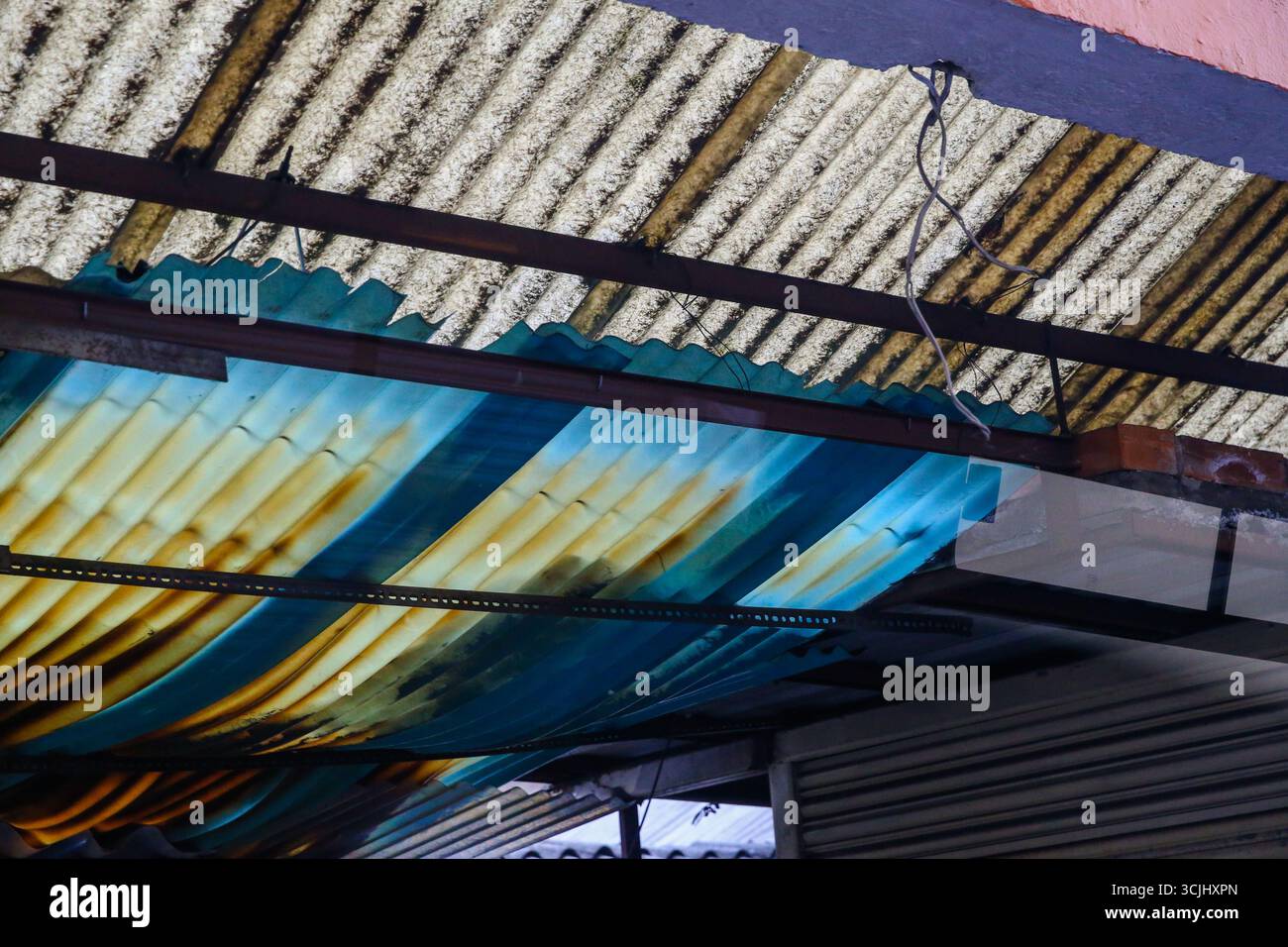 Gros plan abstrait de feuilles de toiture ondulées rouillées avec des panneaux bleus peints et des tuiles de ciment, mettant en valeur les textures urbaines et la pourriture des matériaux. Banque D'Images