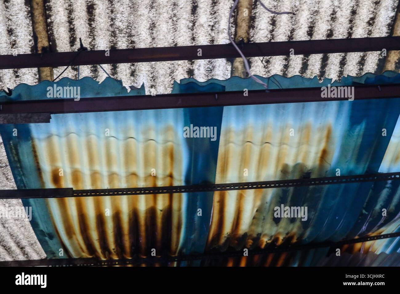 Gros plan abstrait de feuilles de toiture ondulées rouillées avec des panneaux bleus peints et des tuiles de ciment, mettant en valeur les textures urbaines et la pourriture des matériaux. Banque D'Images