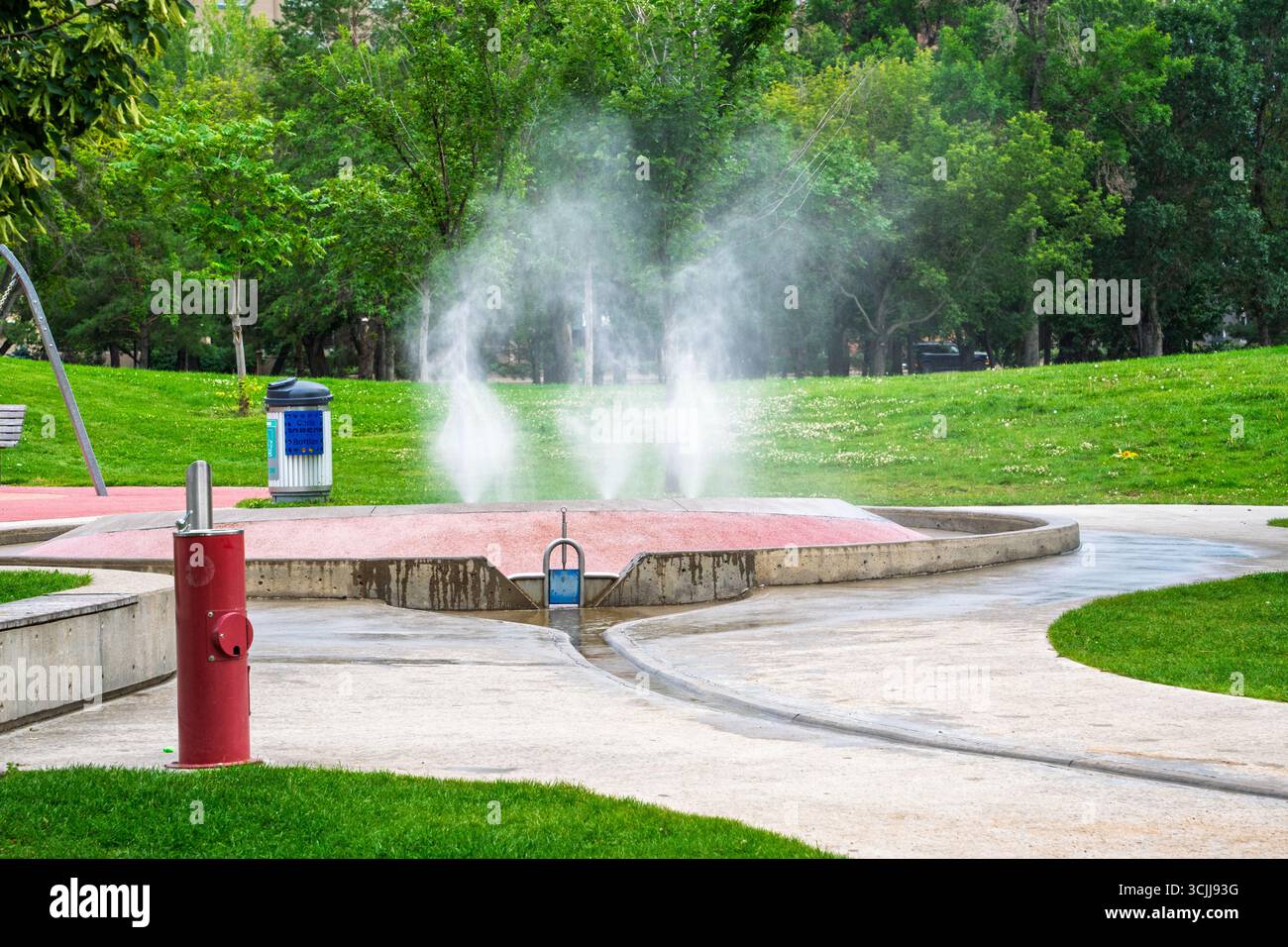 Garez-vous avec une fontaine et une bouche d'incendie. La fontaine pulvérise de l'eau et la bouche d'incendie est rouge Banque D'Images