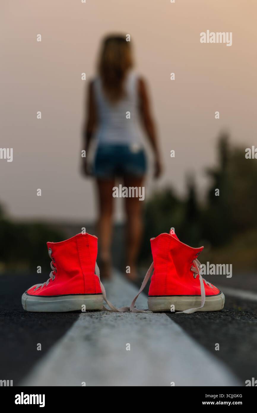 Femme s'éloignant des baskets rouges sur la route Banque D'Images