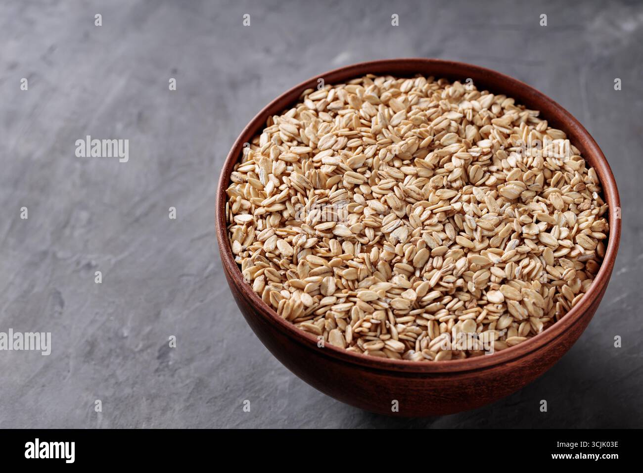 Flocons d'avoine dans un bol en céramique sur un espace de copie de surface grise Banque D'Images