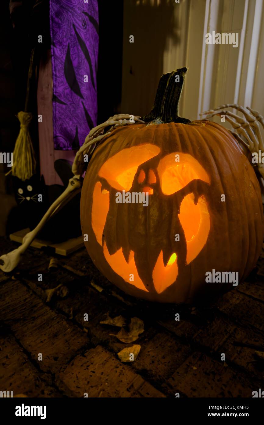 Une citrouille sculptée avec une image d'un fantôme brille avec une bougie orange dans le cadre des décorations d'Halloween d'une maison. Banque D'Images