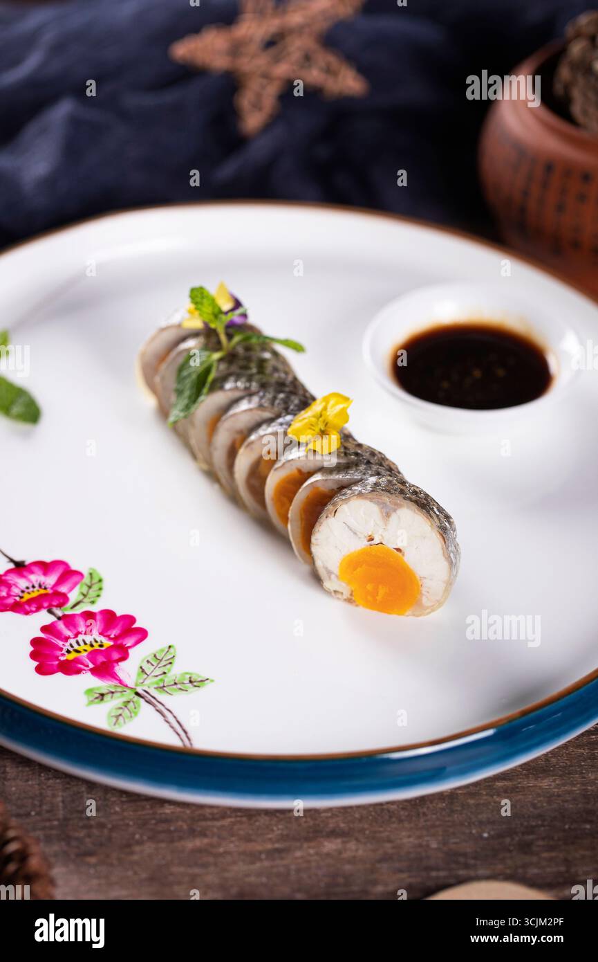 Rouleau de bar de mer au jaune d'oeuf salé avec sauce trempée sur une assiette blanche Banque D'Images