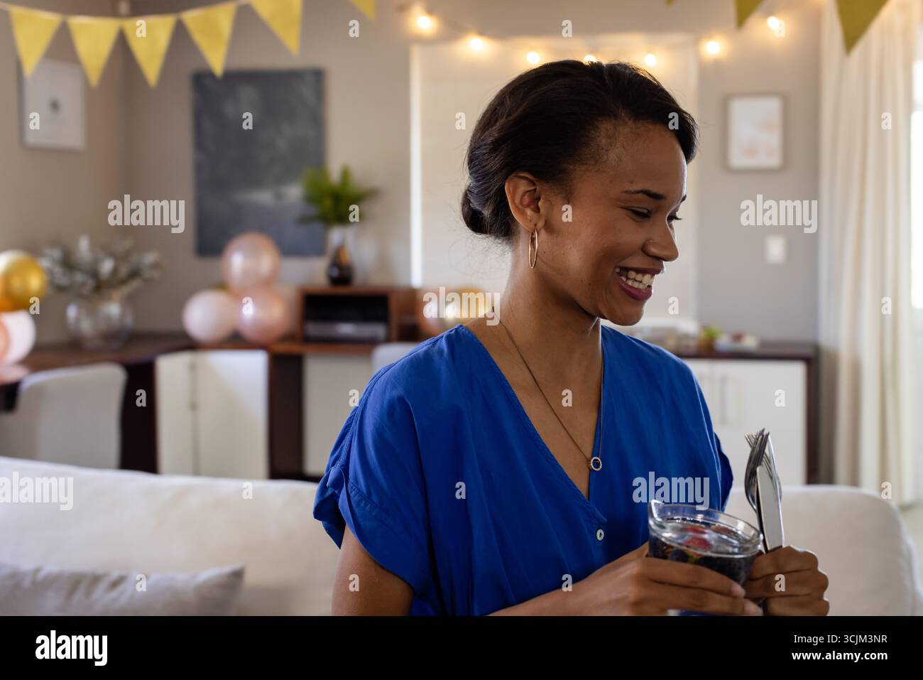 Femme souriante en robe bleue tenant le verre, se préparant à la célébration à la maison Banque D'Images