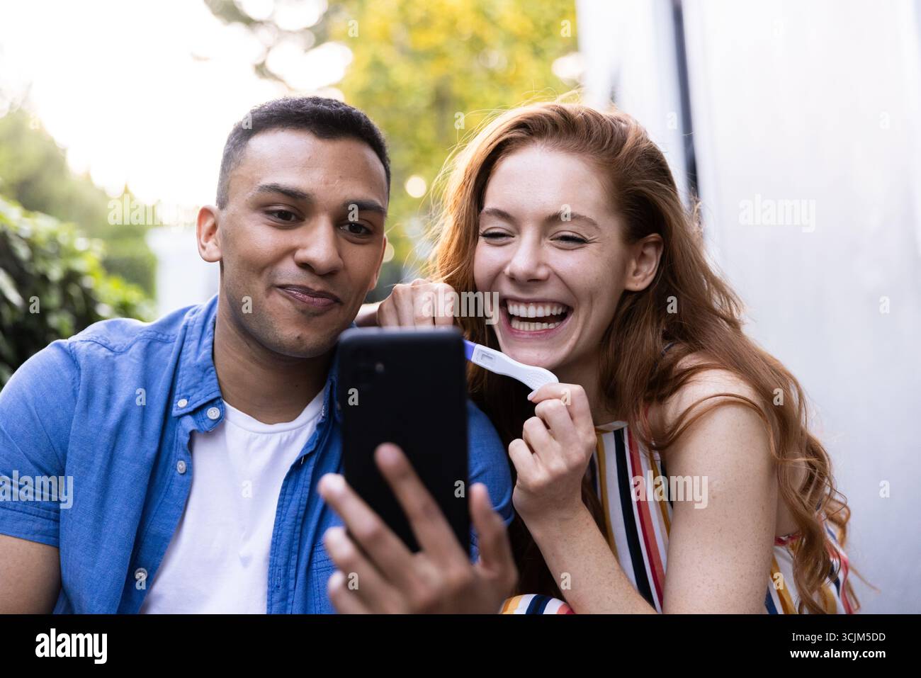 Jeune couple célébrant un résultat positif de test de grossesse pendant un appel vidéo à l'extérieur Banque D'Images