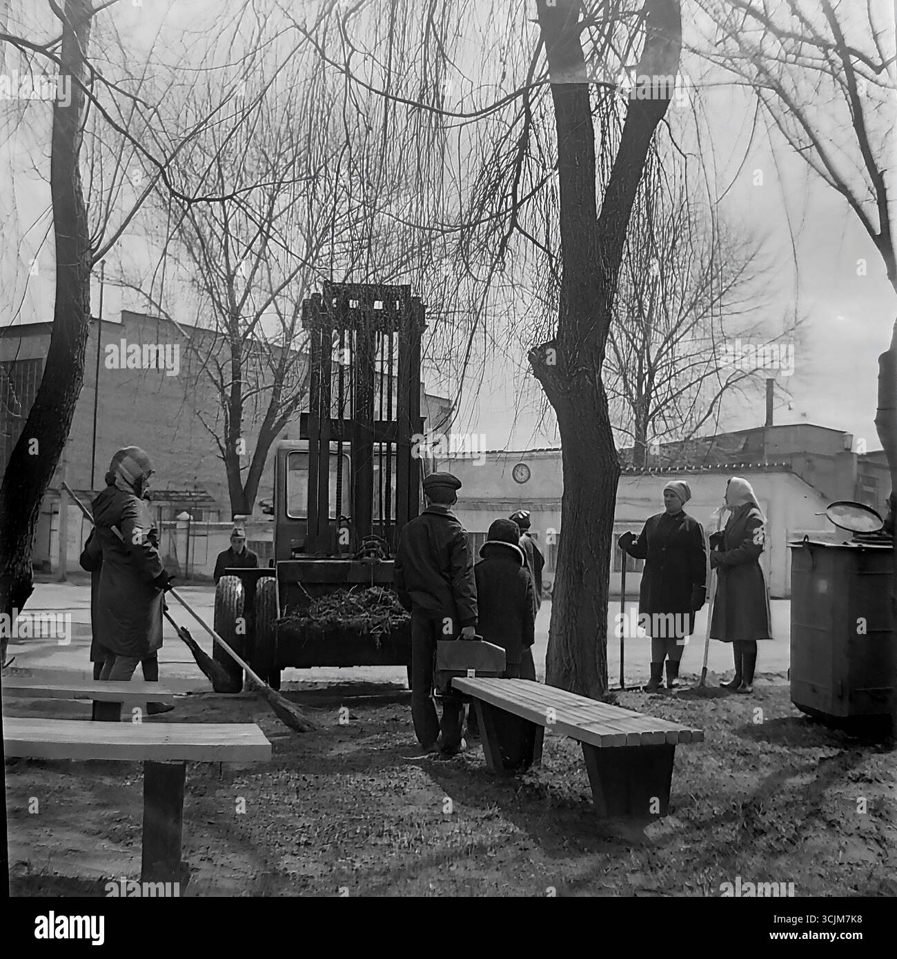 Un Subbotnik printanier dans une usine de Slavyansk en 1974 : des ouvriers, principalement des femmes, se reposent après avoir nettoyé le terrain, tandis qu'un chariot élévateur est chargé de branches et une cuisine de champ se trouve à proximité. Ce cliché, qui capture le rituel du travail collectif de l'époque de la stagnation, est un symbole de camaraderie, d'amélioration de la communauté et de la vie paisible et créative dans le Donbass Banque D'Images