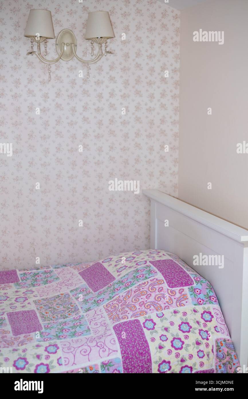 Couvre-lit coloré aux motifs complexes est élégamment placé sur un cadre de lit blanc dans une chambre à coucher légèrement éclairée, créant une atmosphère chaleureuse et accueillante Banque D'Images