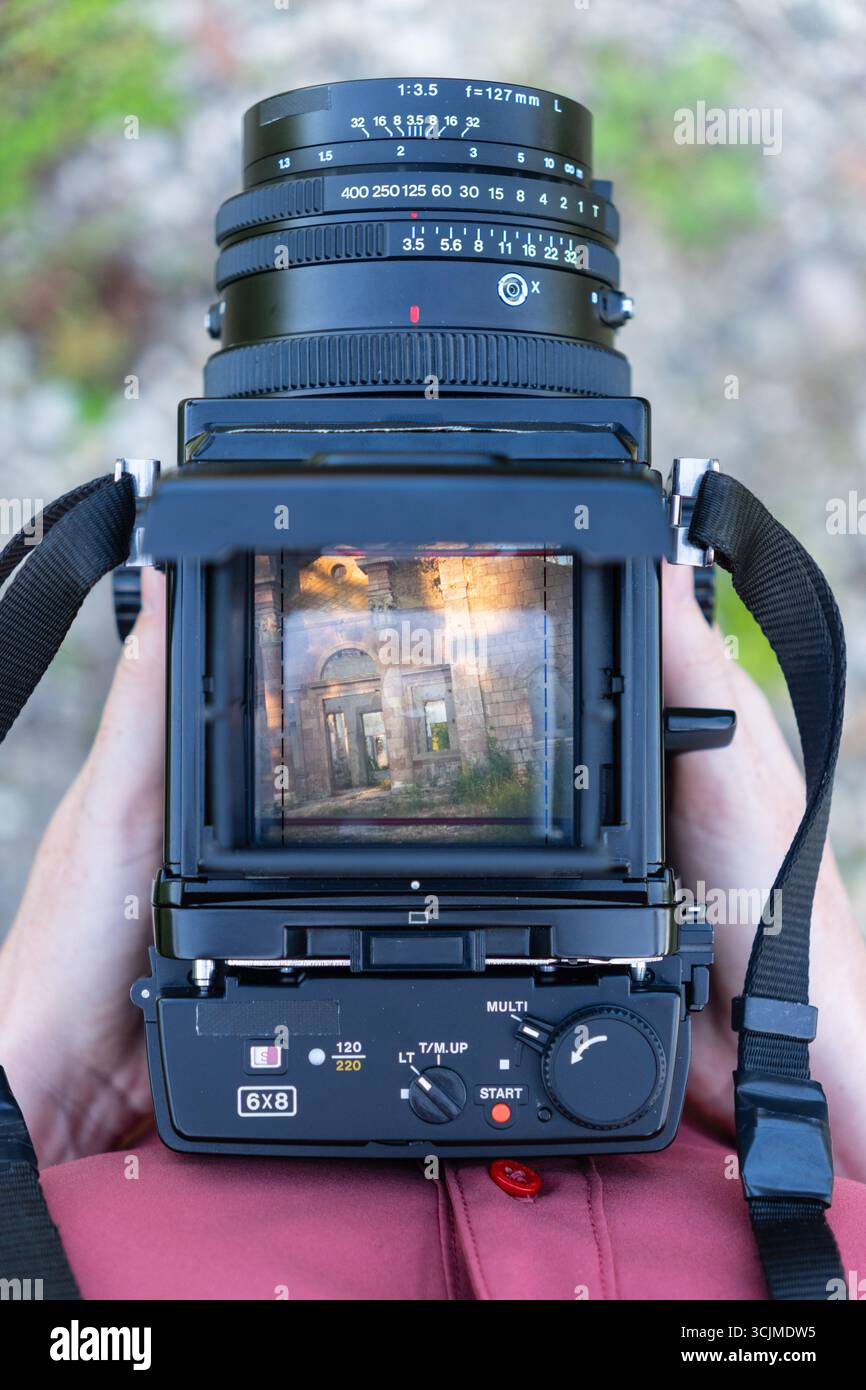 Une femme regarde à travers le viseur d'un appareil photo moyen format vintage. Dans le viseur, il voit le bâtiment antique par une journée ensoleillée Banque D'Images