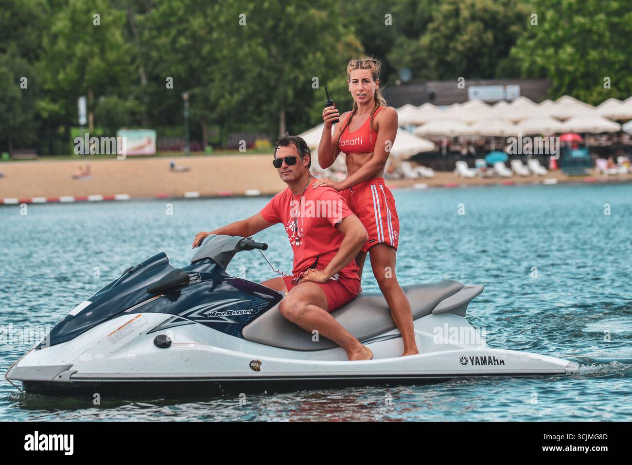 Sauveteur masculin conduisant un jet ski avec sauveteur féminin debout derrière tenant un talkie-walkie sur le lac Banque D'Images